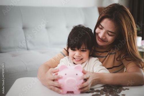 Mother and daughter putting coins into piggy bank. Family budget and savings concept. Junior Savings Account concept