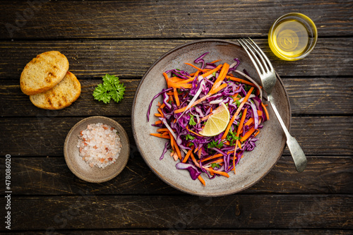 Fresh coleslaw salad made of shredded red and white cabbage and carrots on dark wooden background, top view