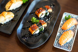 Premium Unagi sushi (Grilled eel) pieces which are served in black plate, placed on wooden table. Japanese food object photo, Close-up and partial focus.