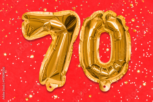 The number of the balloon made of golden foil, the number seventy on a red background with sequins. Birthday greeting card with inscription 70. Anniversary concept. Celebration event. photo