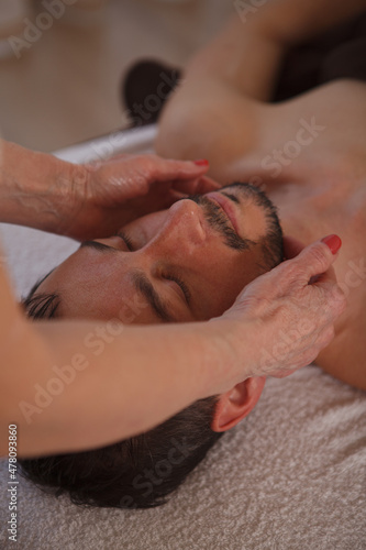 Vertical close up of a mature man enjoying professional face massage at spa salon