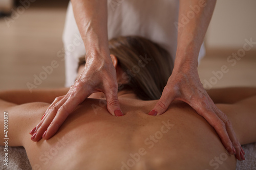 Close up of hands of professional masseuse working at spa, massaging back of female client