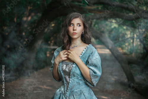 Beautiful young woman in 18-19 century dress and white gloves in the forest by the pond. Girl in a mysterious forest. The photo