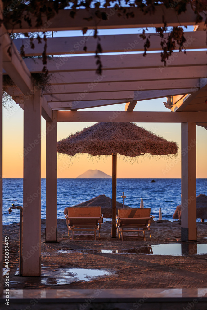 Fototapeta premium Beach chairs and straw parasol at sunset