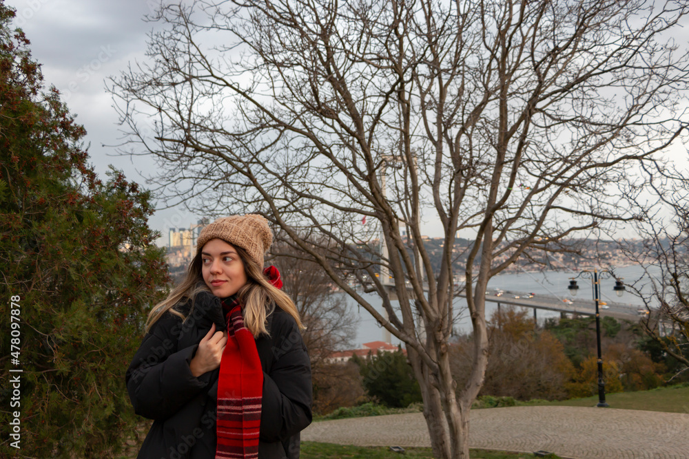 A pretty, happy girl in forest. She is in front of a fallen tree in autumn. She wears winter coat. She has hat and red scarf. She holding her hat and looking sideways. Nature admiration. Fresh air. A pretty, happy girl in forest. She is in front of a fallen tree in autumn. She wears winter coat. She has hat and red scarf. She holding her hat and looking sideways. Nature admiration. Fresh air.