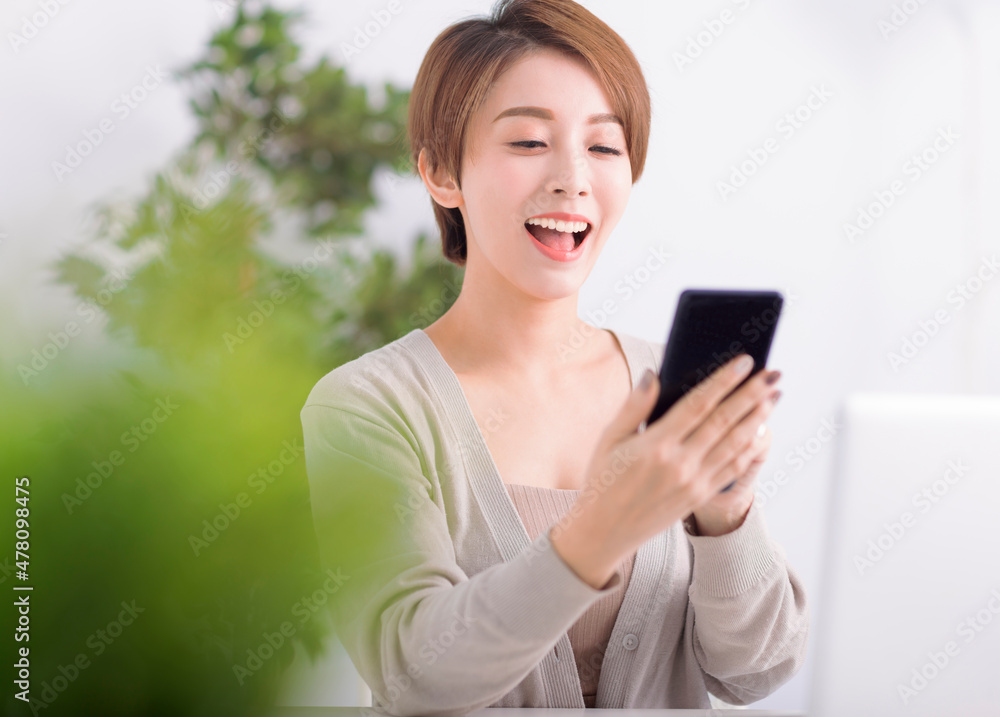 Beautiful excited young woman watching mobile phone in living room Beautiful excited young woman watching mobile phone in living room