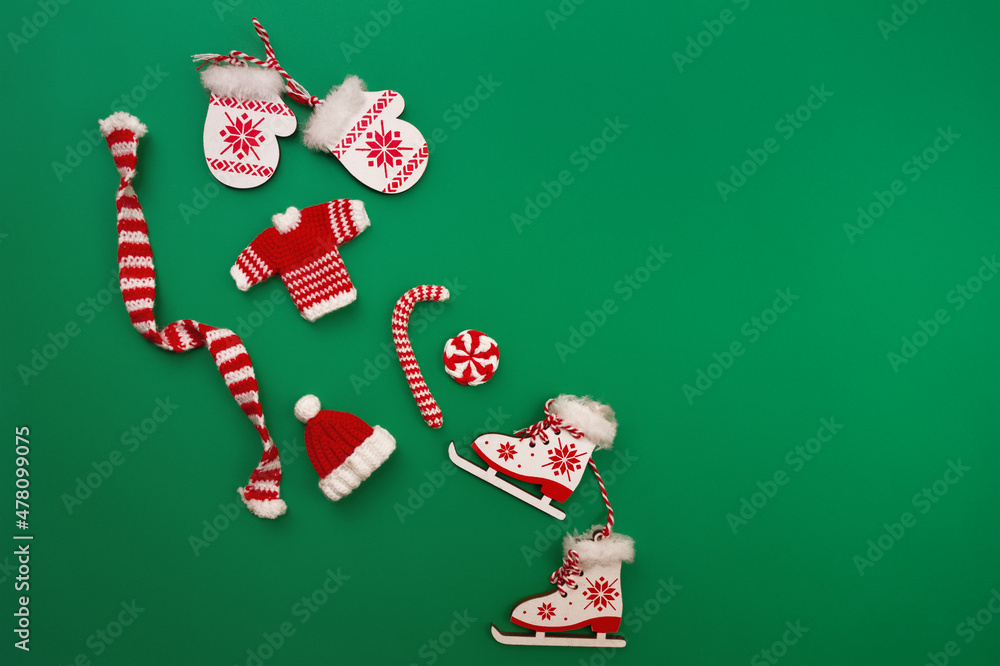 decorative knitted ornaments scarf, sweater, hat and caramel, wooden decorative mittens and skates in red and white color on green background