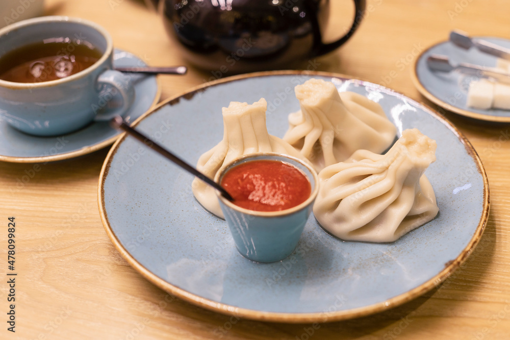 Hot khinkali with tomato, hot sauce on a beautiful plate in a cafe. Georgian cuisine. Soft focus. Hot khinkali with tomato, hot sauce on a beautiful plate in a cafe. Georgian cuisine. Soft focus.