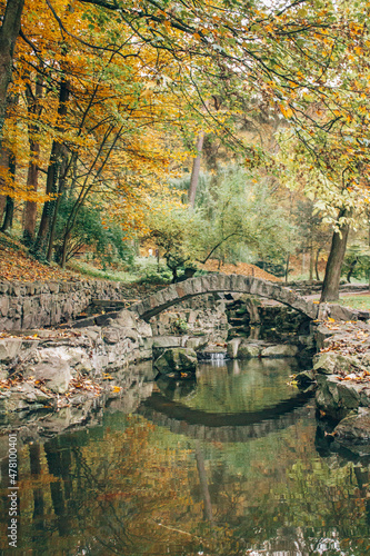 Beautiful autumn park with yellow leaves fallen. Beautiful autumn background landscape with stone bridge across the stream. Colorful foliage falling. Selective focus. Vertical image