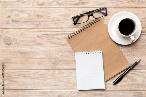 Modern office desk table with notebook and other supplies with cup of coffee. Blank notebook page for you design. Top view  flat lay