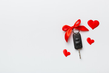 Car key with a red bow and a heart on Colored table. Giving present or gift for valentine day or christmas, Top view with copy space