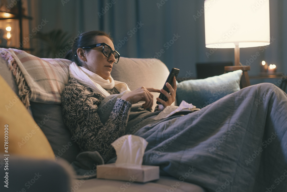 Sick woman resting on the couch and connecting with her smartphone Sick woman resting on the couch and connecting with her smartphone