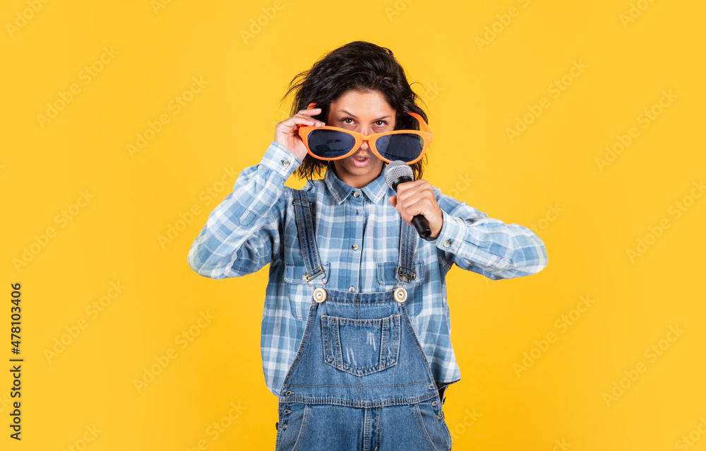cheerful lady in shirt denim style singing in mic on yellow background, party