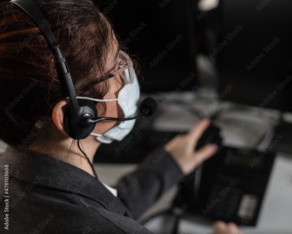 A woman call center operator in a medical mask answers the phone. A woman call center operator in a medical mask answers the phone.