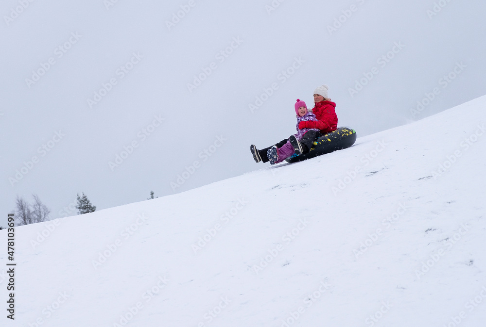 The family goes downhill on an inflatable ring, winter entertainment. A young woman and a child ride down a snowy mountain.
