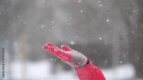 A female hand in a red glove catches snowflakes in winter on a blurred background. Slow motion, shallow depth of field