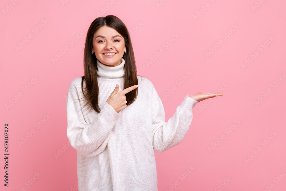 Happy woman presenting copy space on her palm, showing empty place for commercial text or goods, wearing white casual style sweater. Indoor studio shot isolated on pink background. Happy woman presenting copy space on her palm, showing empty place for commercial text or goods, wearing white casual style sweater. Indoor studio shot isolated on pink background.