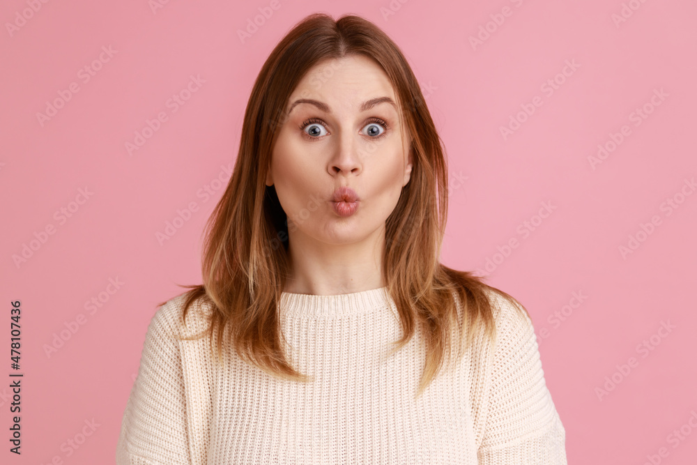 Portrait of blond woman showing fish face grimace with pout lips, fooling around, making ridiculous childish comical grimace, wearing white sweater. Indoor studio shot isolated on pink background. Portrait of blond woman showing fish face grimace with pout lips, fooling around, making ridiculous childish comical grimace, wearing white sweater. Indoor studio shot isolated on pink background.