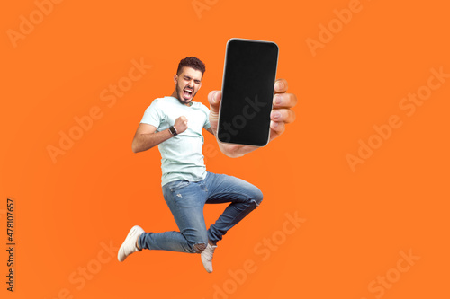 Fototapeta Happy man flying and jumping in air and showing big mobile empty screen for copy space and advertising area