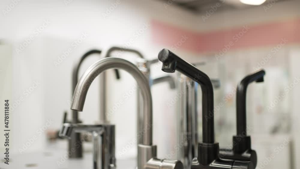 Wide selection of metal and steel faucets standing on counter in hardware store for home repairing and renovations against blurred background Wide selection of metal and steel faucets standing on counter in hardware store for home repairing and renovations against blurred background