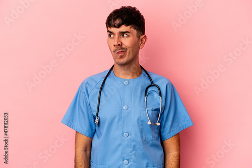 Young mixed race nurse man isolated on pink background confused, feels doubtful and unsure.