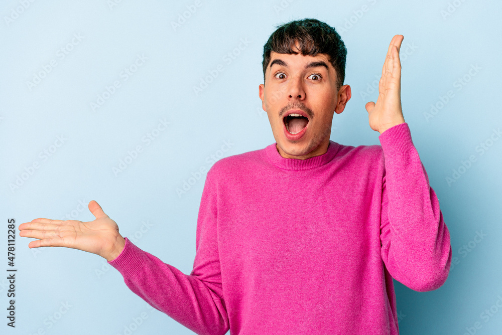 Young mixed race man isolated on blue background holds copy space on a palm, keep hand over cheek. Amazed and delighted. Young mixed race man isolated on blue background holds copy space on a palm, keep hand over cheek. Amazed and delighted.