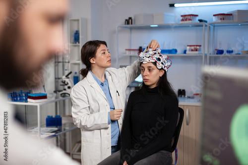 Neurologist researcher doctor adjusting eeg scanner on patient head analyzing brain evolution working at disease diagnosis during neurology experiment in high tech lab. Doctor explaining tomography