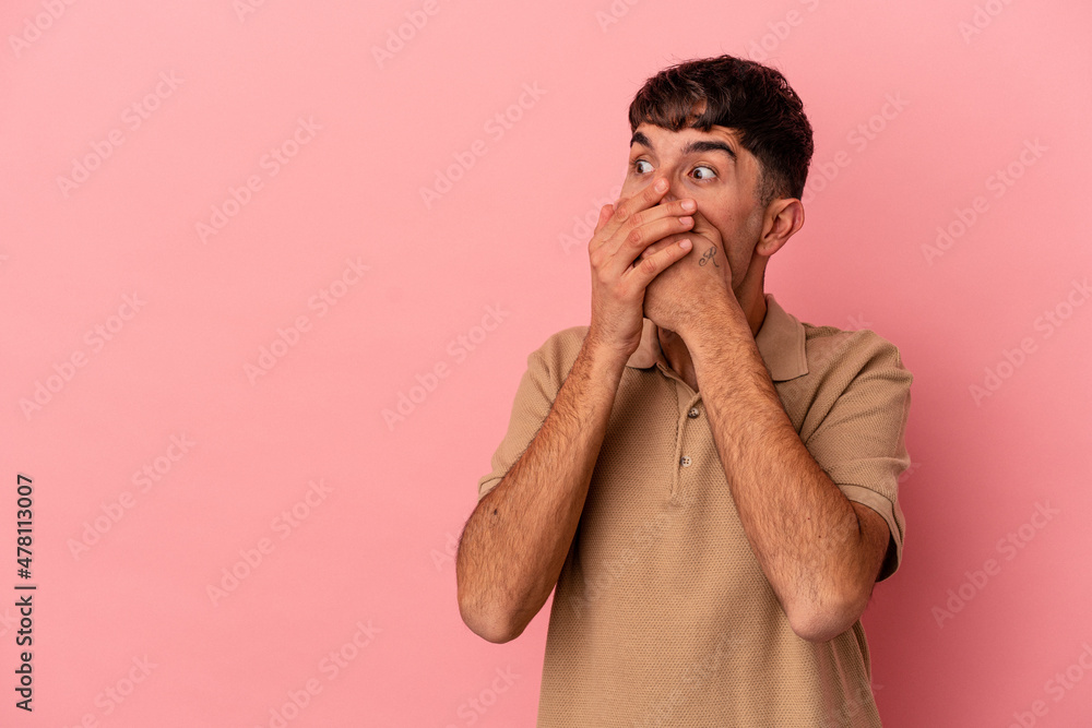 Young mixed race man isolated on pink background thoughtful looking to a copy space covering mouth with hand. Young mixed race man isolated on pink background thoughtful looking to a copy space covering mouth with hand.