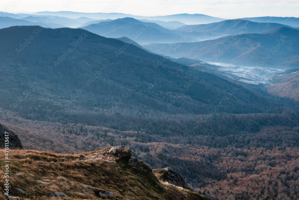 Amazing landscape of mountains layers range at hazy morning. A view of the misty slopes of the mountains in the distance and forest hills  in rays of sunlight. 