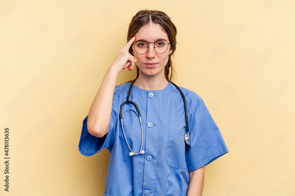 Young nurse caucasian woman isolated on yellow background pointing temple with finger, thinking, focused on a task. Young nurse caucasian woman isolated on yellow background pointing temple with finger, thinking, focused on a task.