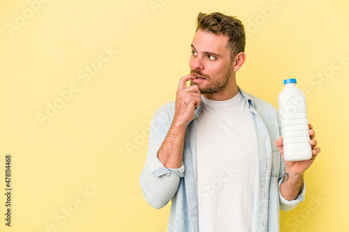 Young caucasian man holding a bottle of milk isolated on yellow background relaxed thinking about something looking at a copy space.