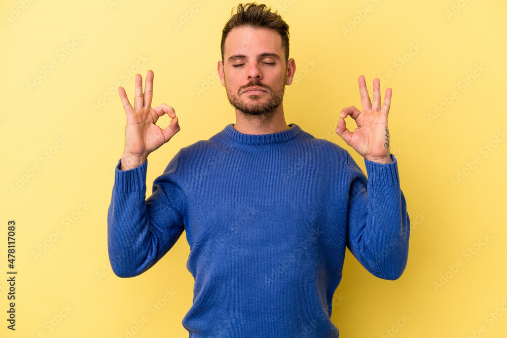 Fototapeta premium Young caucasian man isolated on yellow background relaxes after hard working day, she is performing yoga.