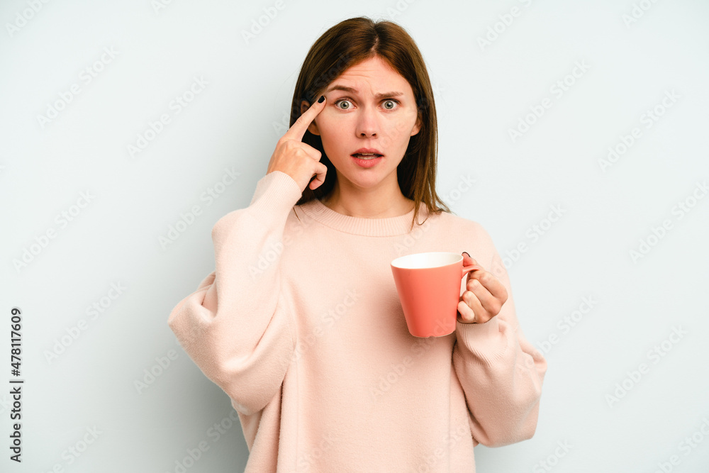 Young English woman holding a mug isolated on blue background showing a disappointment gesture with forefinger. Young English woman holding a mug isolated on blue background showing a disappointment gesture with forefinger.