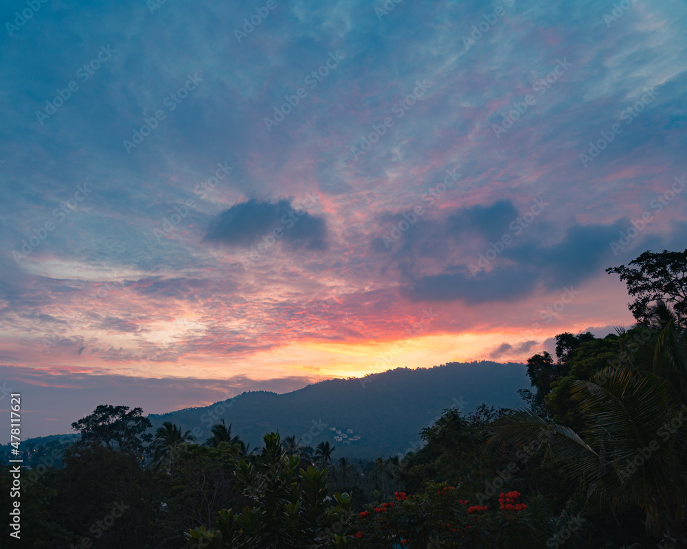 Colorful sunset sky over tress and mountain on a tropical island in a summer evening. View from the top.