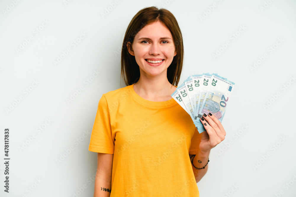 Young English woman holding banknotes isolated on blue background happy, smiling and cheerful. Young English woman holding banknotes isolated on blue background happy, smiling and cheerful.