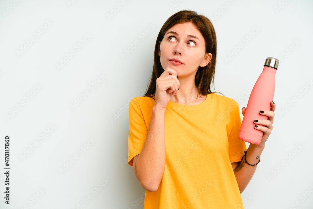 Young English woman holding a thermo isolated on blue background looking sideways with doubtful and skeptical expression. Young English woman holding a thermo isolated on blue background looking sideways with doubtful and skeptical expression.