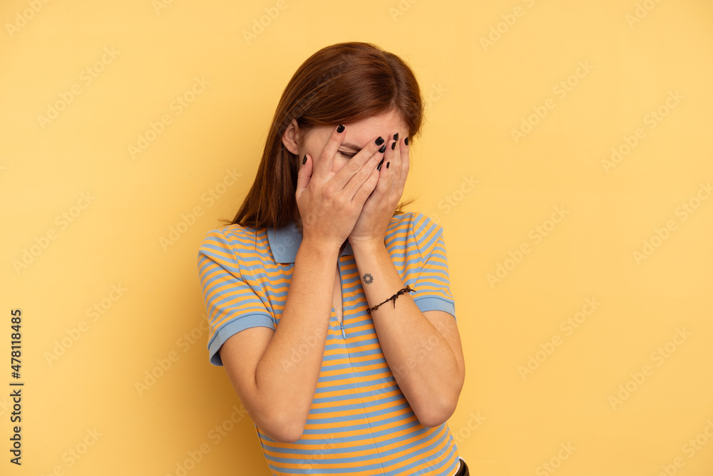 Young English woman isolated on yellow background blink at the camera through fingers, embarrassed covering face. Young English woman isolated on yellow background blink at the camera through fingers, embarrassed covering face.