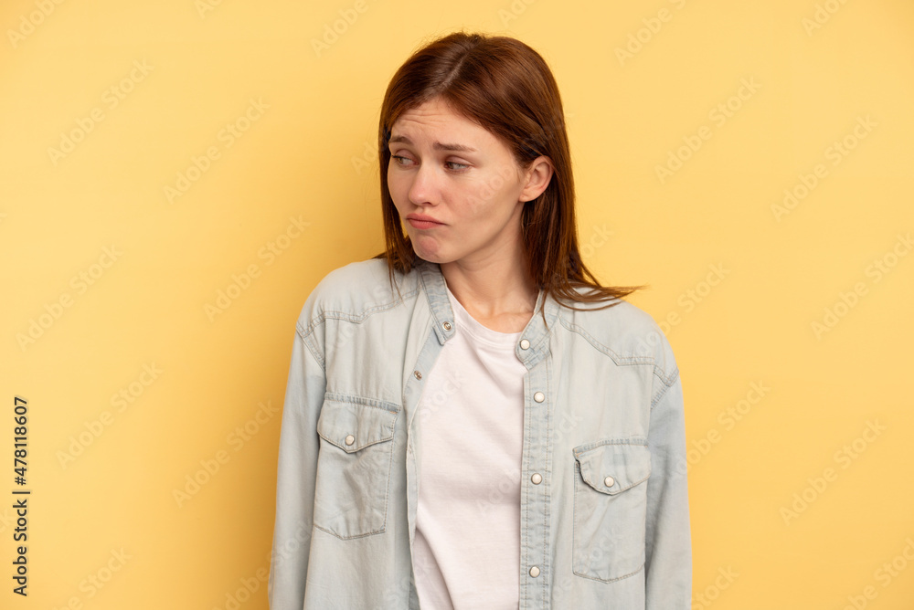 Young English woman isolated on yellow background shrugs shoulders and open eyes confused. Young English woman isolated on yellow background shrugs shoulders and open eyes confused.
