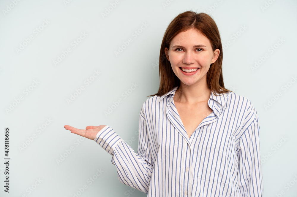Young English woman isolated on blue background showing a copy space on a palm and holding another hand on waist. Young English woman isolated on blue background showing a copy space on a palm and holding another hand on waist.