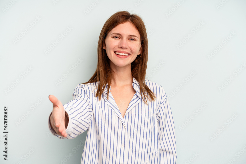 Young English woman isolated on blue background stretching hand at camera in greeting gesture. Young English woman isolated on blue background stretching hand at camera in greeting gesture.