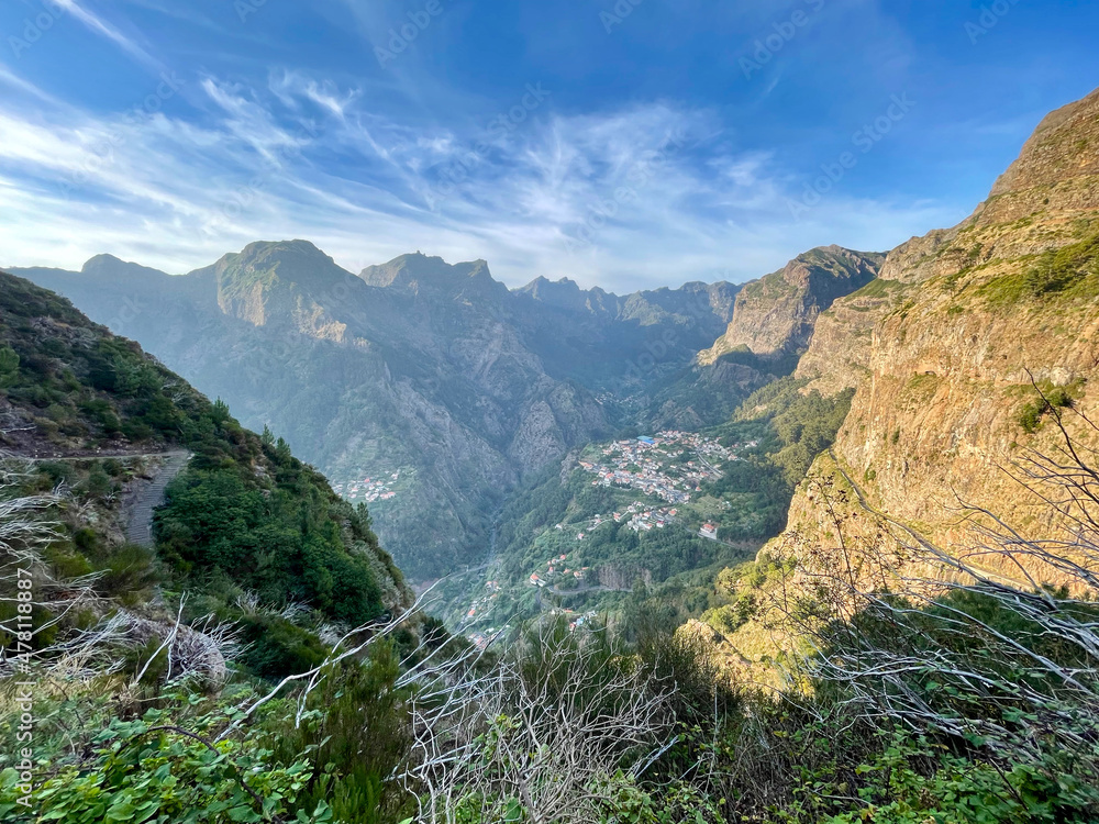 Obraz premium View of a vast valley surrounded by green hills in the light of the setting sun and with a blue sky in the background, Madeira, Portugal