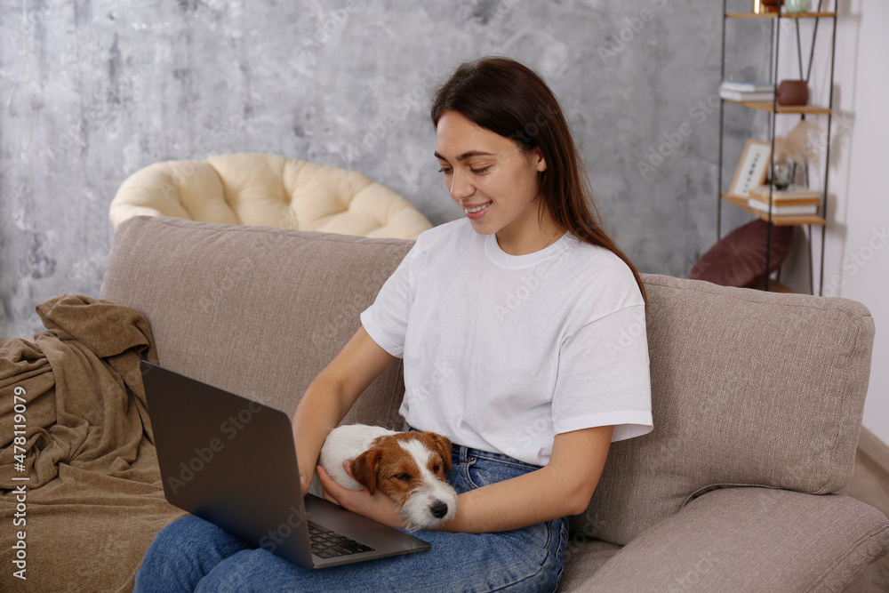 Portrait of young beautiful hipster woman working on a laptop with her adorable wire haired Jack Russel terrier puppy at home. Female with rough coated pup. Interior background, close up, copy space. Portrait of young beautiful hipster woman working on a laptop with her adorable wire haired Jack Russel terrier puppy at home. Female with rough coated pup. Interior background, close up, copy space.
