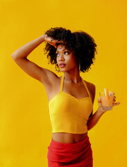beautiful young African american woman in bright summer outfit drinking refreshing cocktail isolated on yellow background