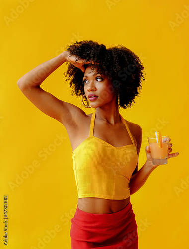 beautiful young African american woman in bright summer outfit drinking refreshing cocktail isolated on yellow background