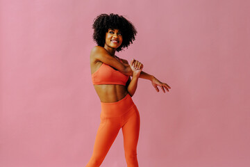 beautiful smiling young fit woman in sportswear stretching isolated on pink background