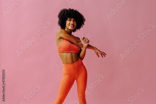 beautiful smiling young fit woman in sportswear stretching isolated on pink background photo