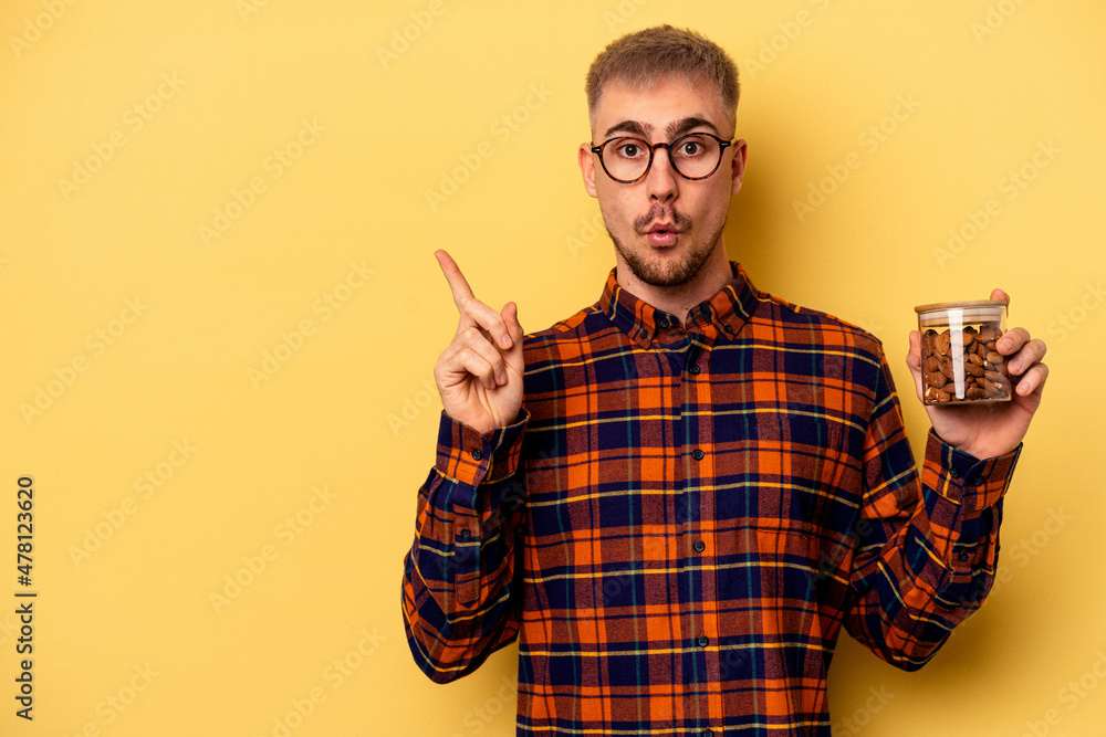 Fototapeta premium Young caucasian man holding a almond jar isolated on yellow background pointing to the side