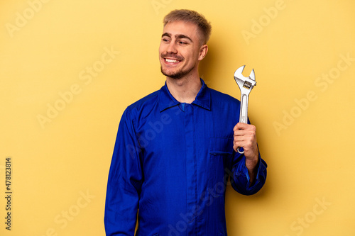 Young electrician caucasian man isolated on yellow background looks aside smiling, cheerful and pleasant.