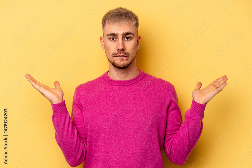 Young caucasian man isolated on yellow background confused and doubtful shrugging shoulders to hold a copy space. Young caucasian man isolated on yellow background confused and doubtful shrugging shoulders to hold a copy space.