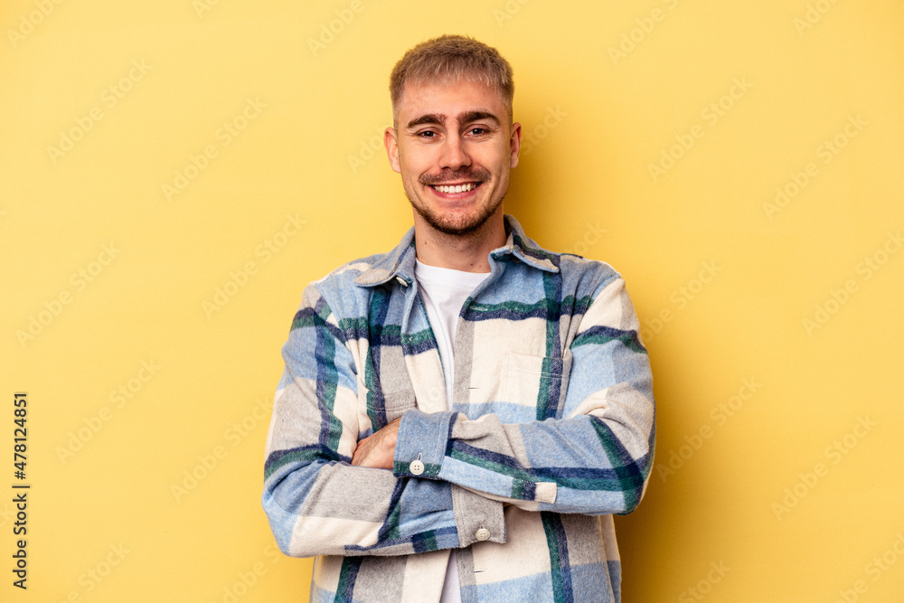 Young caucasian man isolated on yellow background who feels confident, crossing arms with determination. Young caucasian man isolated on yellow background who feels confident, crossing arms with determination.
